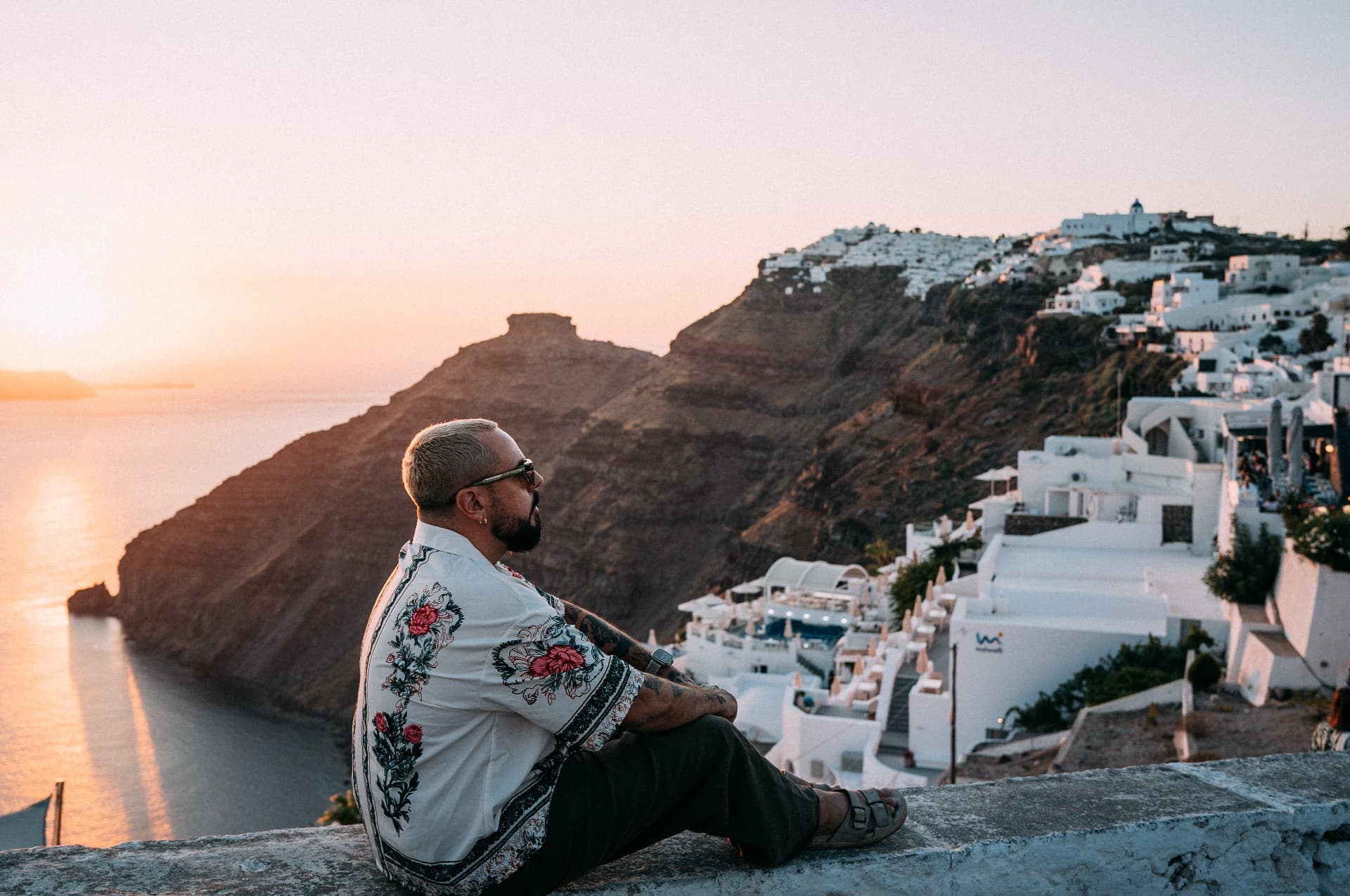 Marc Isla assis de profil sur un muret, face à la mer au coucher du soleil