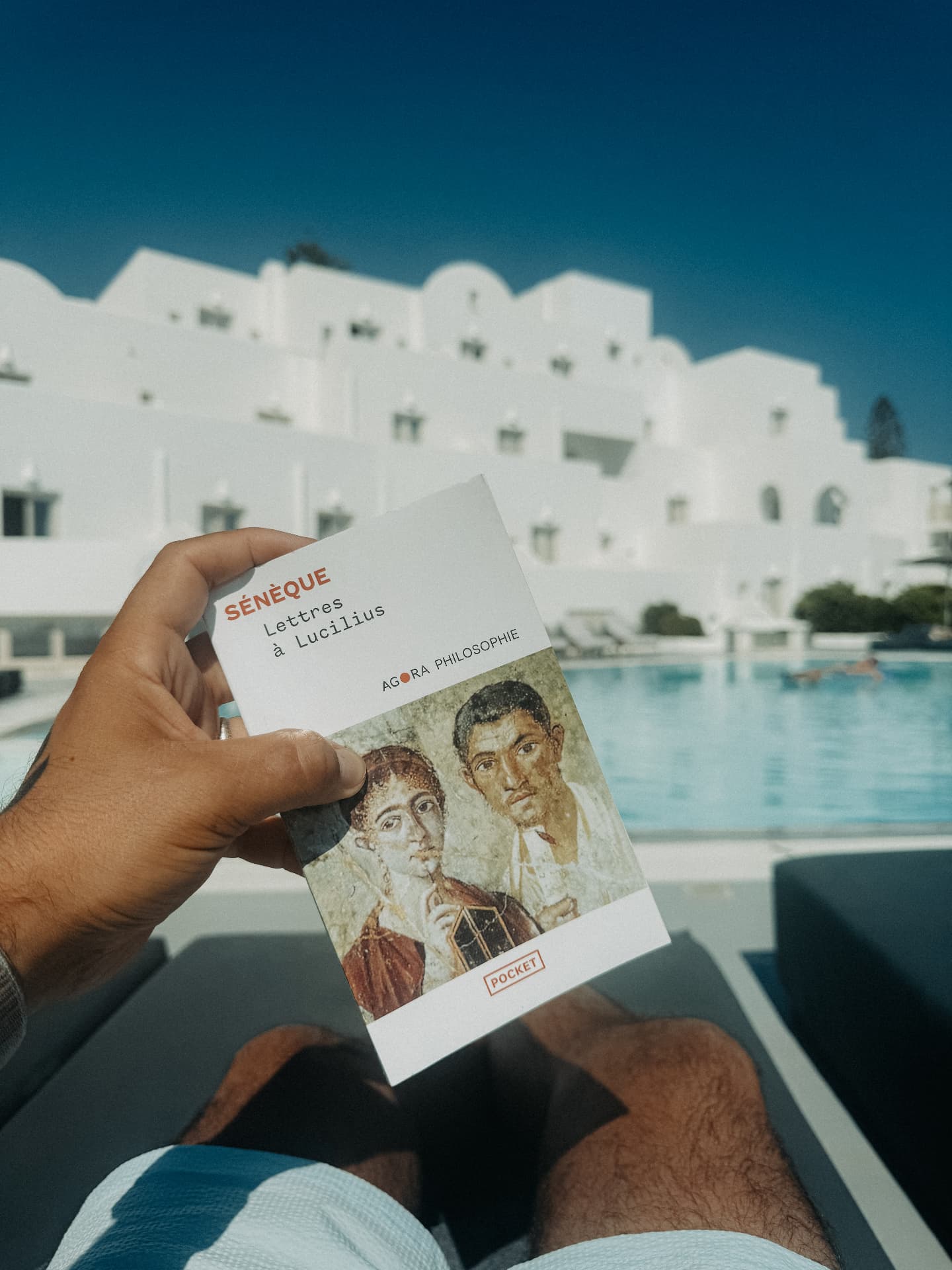 Lettres à Lucilius de Sénèque tenu à la main devant une piscine à Santorin